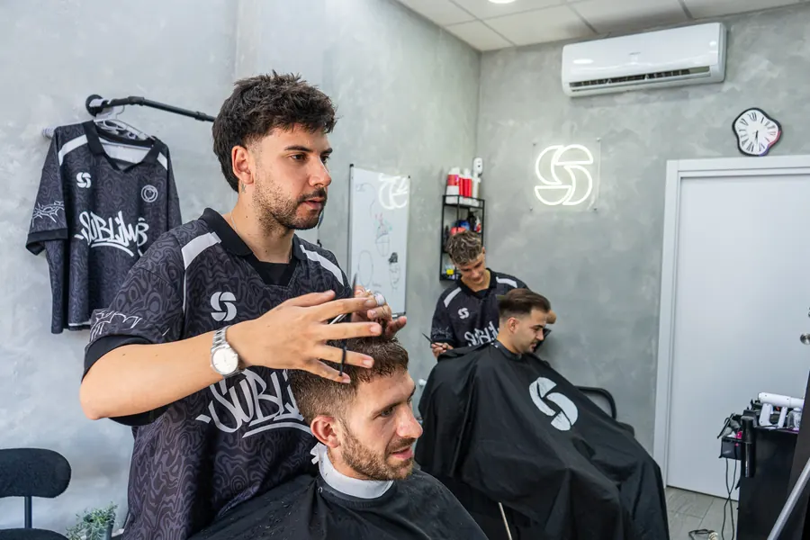 Javi peinando a un cliente bajo el neón de Sublime, con Adri trabajando al fondo