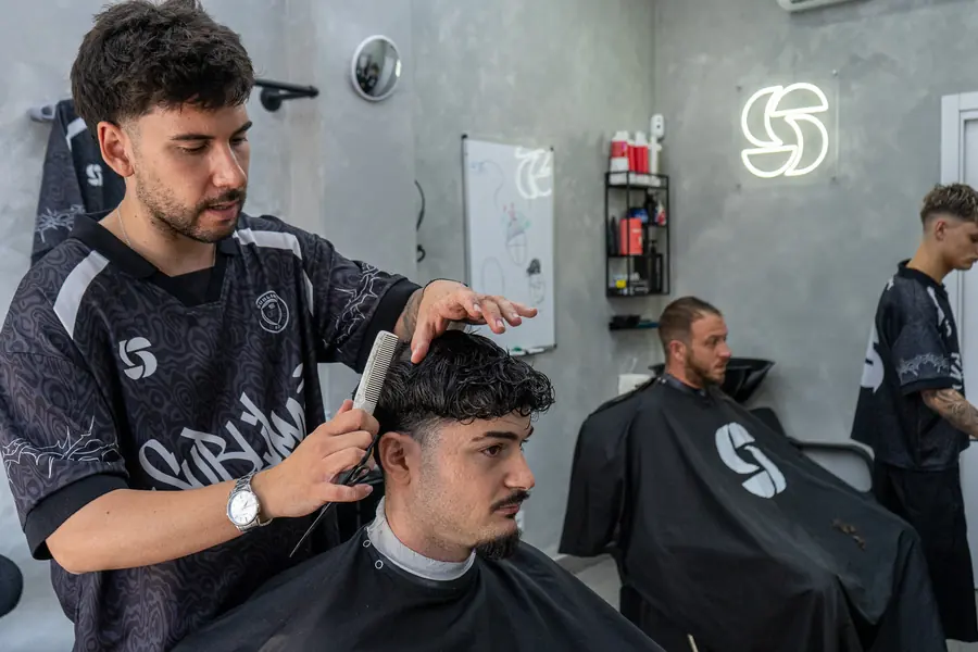 Javi peinando a un cliente mientras Adri trabaja al fondo